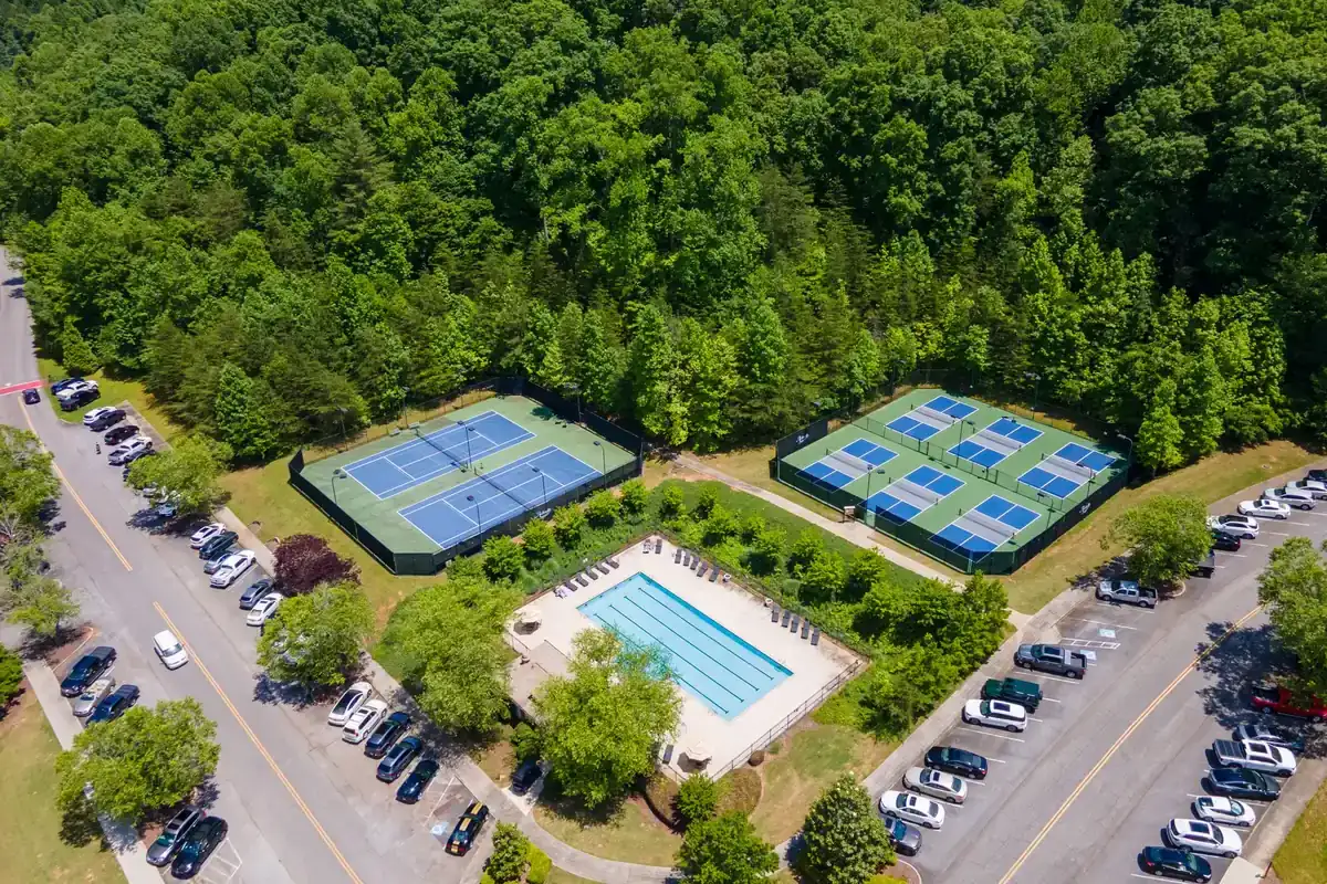 Aerial view of the Achasta amenity area: a lap pool, blue tennis courts and two rows of blue pickleball courts ringed by hardwood forest