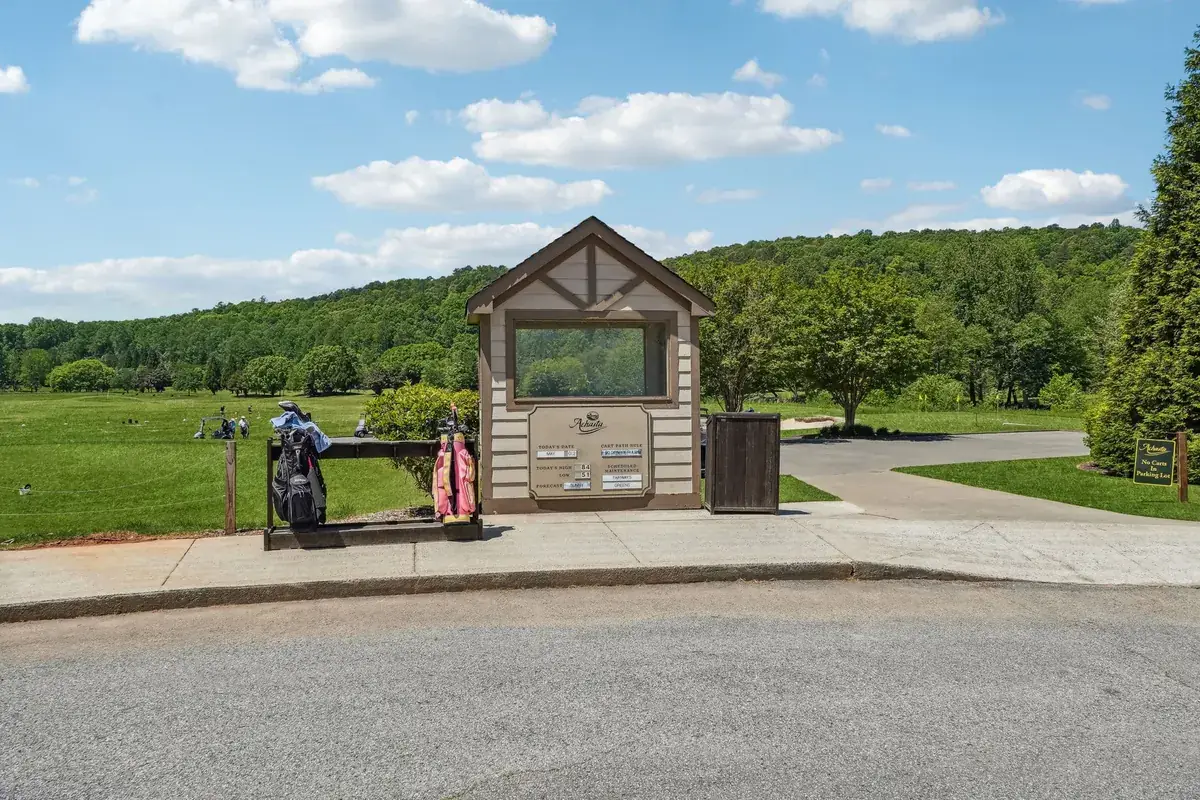 Golf course starter station with golf bags beside a wooded fairway at Achasta